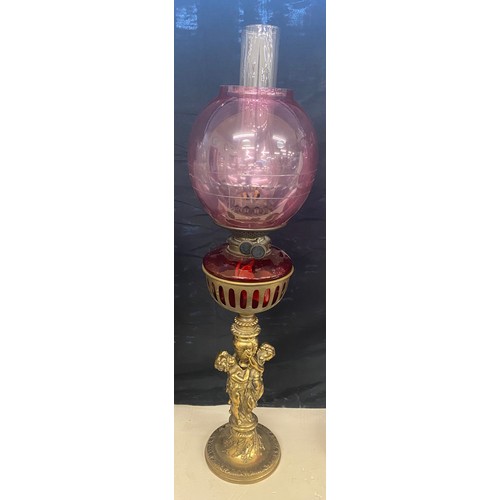 100A - Brass oil lamp, cranberry shade and font with cherubs, approximate height 28 inches