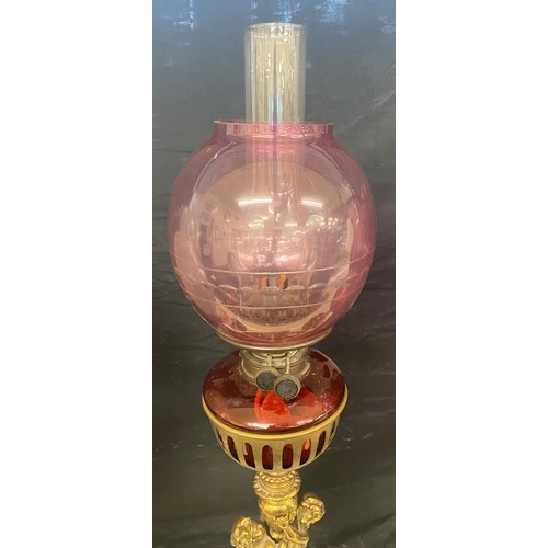 100A - Brass oil lamp, cranberry shade and font with cherubs, approximate height 28 inches