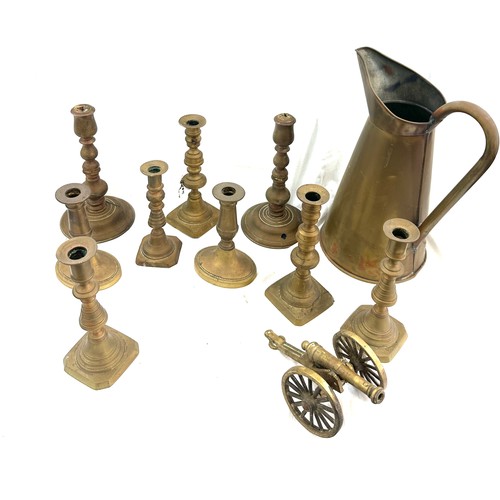 113 - Selection of antique and later brass candle sticks and a large water jug, canon ornament