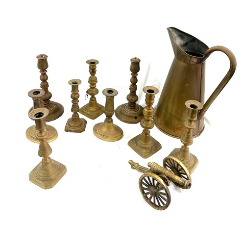 113 - Selection of antique and later brass candle sticks and a large water jug, canon ornament