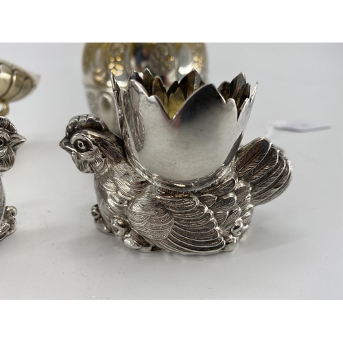 73 - A pair of white metal egg cups in the form of cast chickens with gilt interiors, and a white metal s... 