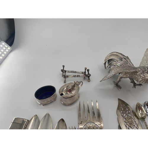 94 - A collection of silver plated and white metal items to include a pair of cast fighting cocks, cutler... 