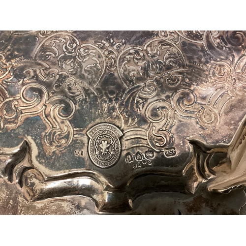 20 - A Sterling silver salver with chased scrolling design and cast bolder raised on three feet by Goldsm... 