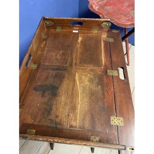 587 - A mahogany and brass hinged folding  butlers tray on a folding stand; and a worn red lacquered shape... 