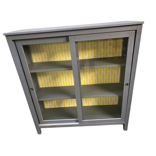 436 - Modern grey painted sliding glazed door bookcase, and yellow patterned design to inside back 120cm W... 