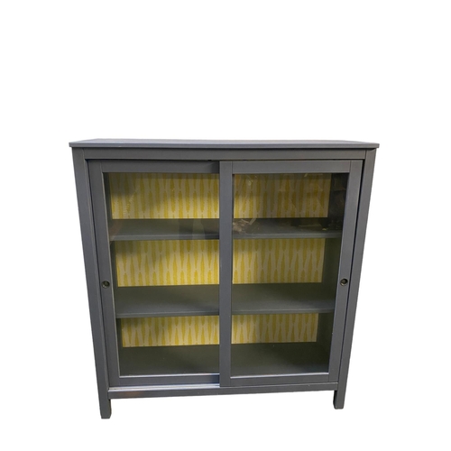 436 - Modern grey painted sliding glazed door bookcase, and yellow patterned design to inside back 120cm W... 