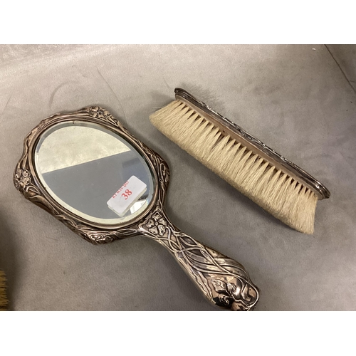 38 - A Sterling silver hand mirror, with Art Nouveau decoration, and three silver mounted brushes of diff... 