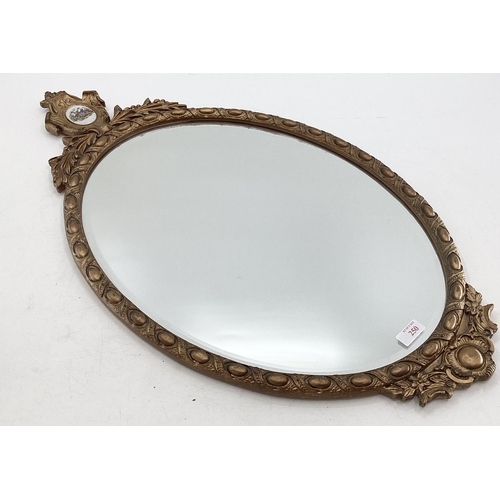 250 - A gilt framed oval mirror, topped by inset ceramic oval panel, bevelled plate, 43-78cm