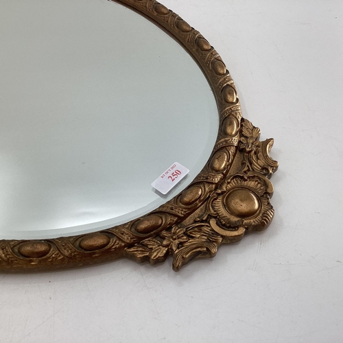 250 - A gilt framed oval mirror, topped by inset ceramic oval panel, bevelled plate, 43-78cm