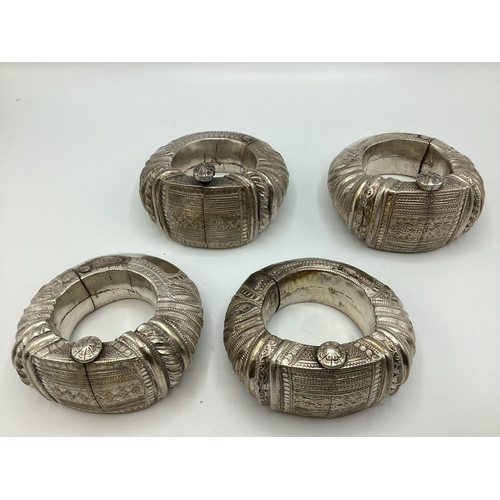 76 - Four middle eastern ornamental slave bangles with chased and beadwork decoration