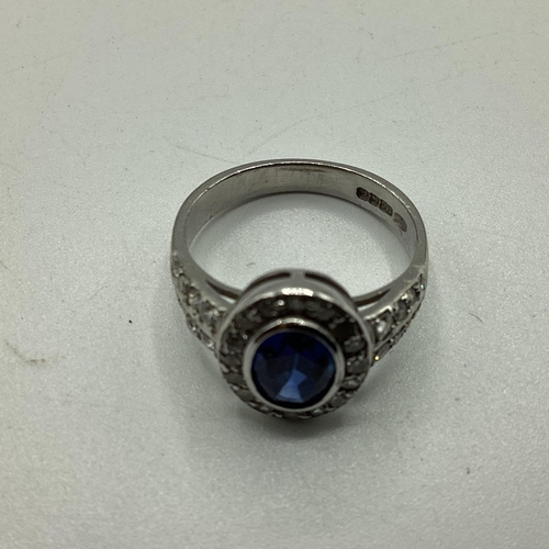 7 - A 18ct white gold sapphire and diamond ring, central oval free cut sapphire in a rub over setting wi... 