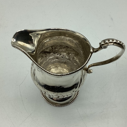 79 - A sterling silver cream jug with repoussé decoration on a beaded circular foot 103 g