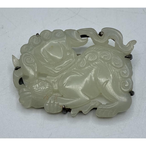 175 - An Oriental jade plaque brooch of a stylised temple lion. with white metal mount. 45mmx 35mm.