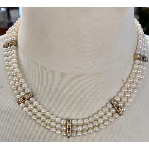 80 - A triple strand of uniform cultured pearls with diamond and ruby set yellow metal separators and unm... 