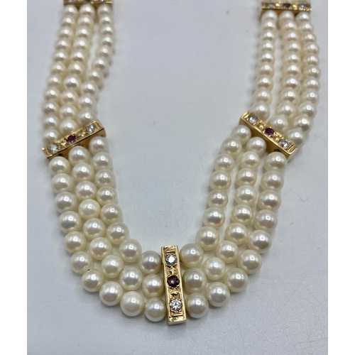 80 - A triple strand of uniform cultured pearls with diamond and ruby set yellow metal separators and unm... 