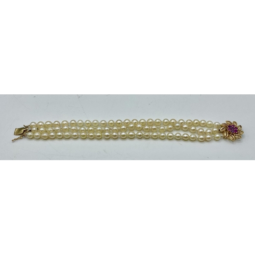 177 - A triple strand uniform pearl bracelet on a 14k gold clasp set with single cut rubies. 20cm.