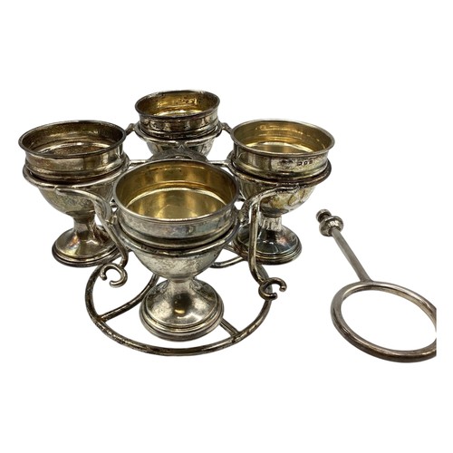 71 - A sterling silver egg cup holder with four egg cups and two spoons(two missing) on a sterling silver... 