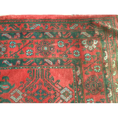 710 - A very large red ground rug with green floral stylized pattern and borders, some all over wear and s... 