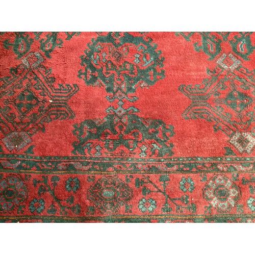 710 - A very large red ground rug with green floral stylized pattern and borders, some all over wear and s... 