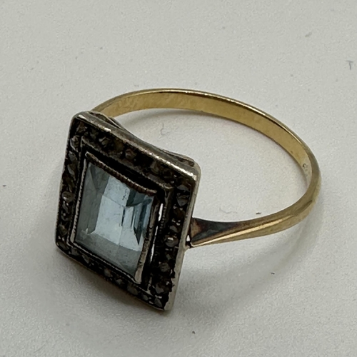 23 - An unmarked yellow metal aquamarine and diamond dress ring. Central emerald cut aquamarine with a su... 