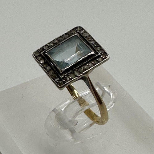 23 - An unmarked yellow metal aquamarine and diamond dress ring. Central emerald cut aquamarine with a su... 