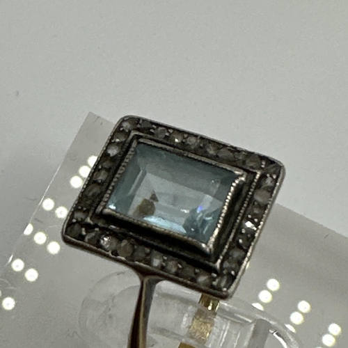 23 - An unmarked yellow metal aquamarine and diamond dress ring. Central emerald cut aquamarine with a su... 