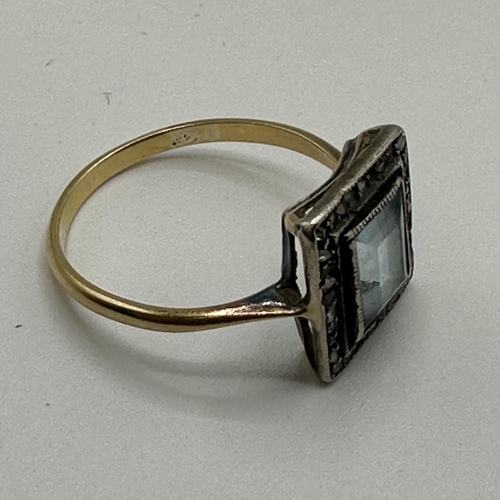 23 - An unmarked yellow metal aquamarine and diamond dress ring. Central emerald cut aquamarine with a su... 