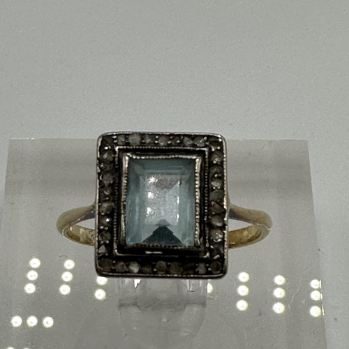 23 - An unmarked yellow metal aquamarine and diamond dress ring. Central emerald cut aquamarine with a su... 