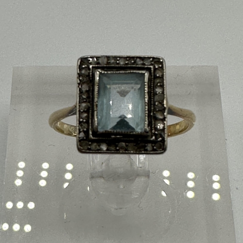 23 - An unmarked yellow metal aquamarine and diamond dress ring. Central emerald cut aquamarine with a su... 