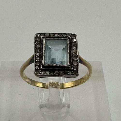 23 - An unmarked yellow metal aquamarine and diamond dress ring. Central emerald cut aquamarine with a su... 