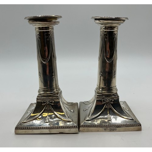 37 - A pair of sterling silver weighted candlesticks, swag and bow design on square bases. Thomas Bradbur... 