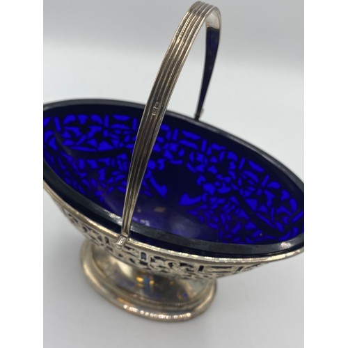 119 - A sterling silver oval swing handle bowl with pierced decoration and blue glass liner by George Nath... 