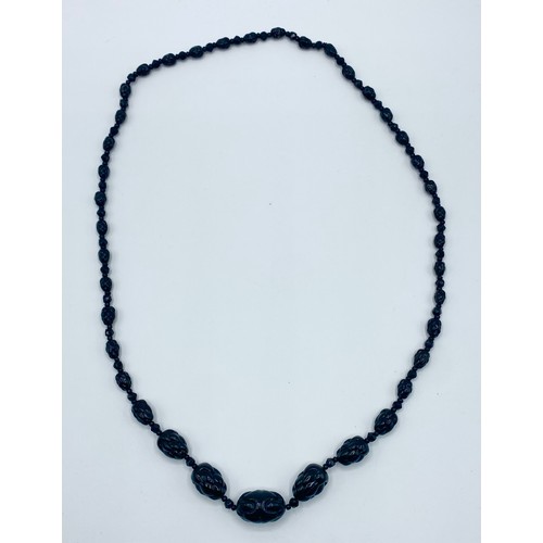 31 - A graduated strand of jet carved beads. 74cm.