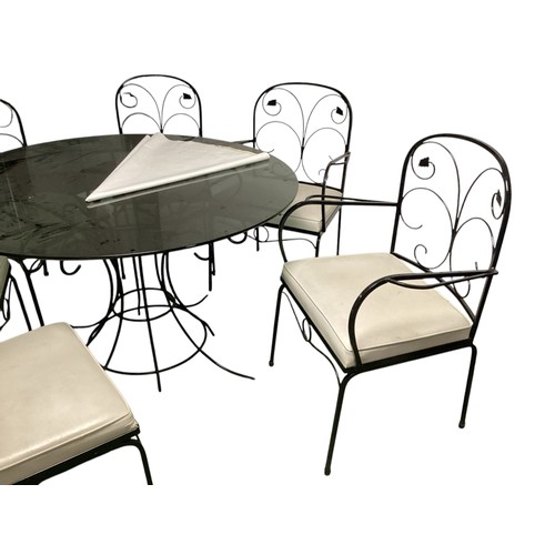 569 - A circular black glass conservatory table  with 6 matching chairs and cushions