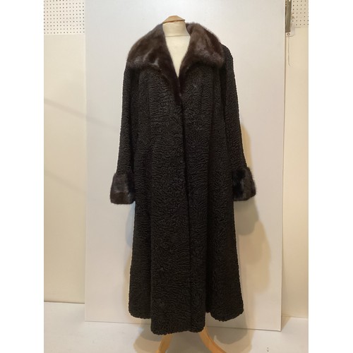 93 - A long, black Astrakhan coat with brown fur collar and cuffs, labelled SWAKARA. Condition, no sign o... 