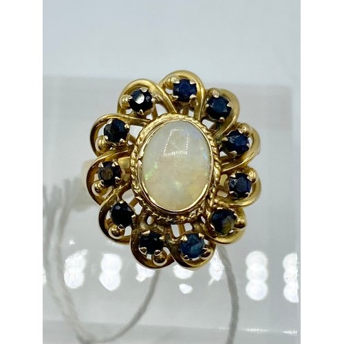 299 - An unmarked yellow metal opal and sapphire dress ring, central cabochon opal with surround of 12 sin... 