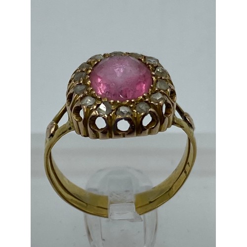 334 - An unmarked yellow metal pink stone ring. Central oval free cut stone with heavily worn facets(unabl... 