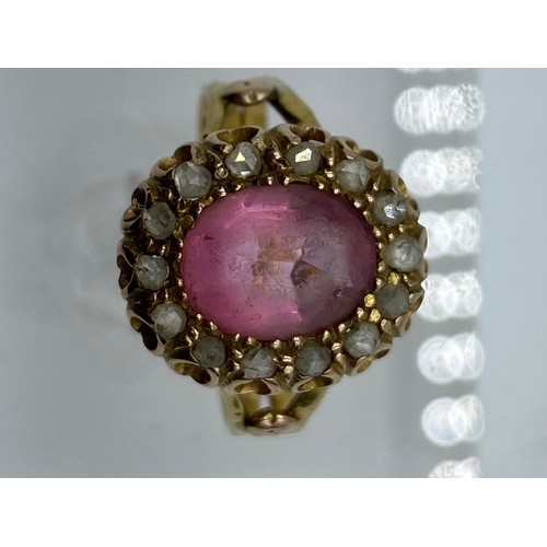 334 - An unmarked yellow metal pink stone ring. Central oval free cut stone with heavily worn facets(unabl... 