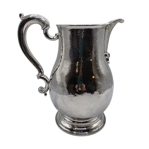 4 - A large Sterling silver hand planished water jug with cast scrolling handle on circular stepped foot... 