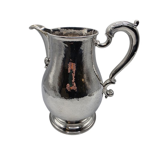 4 - A large Sterling silver hand planished water jug with cast scrolling handle on circular stepped foot... 