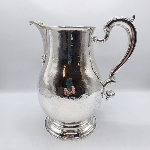 4 - A large Sterling silver hand planished water jug with cast scrolling handle on circular stepped foot... 