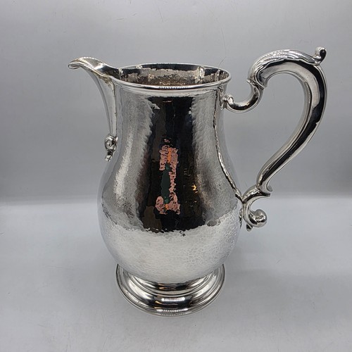 4 - A large Sterling silver hand planished water jug with cast scrolling handle on circular stepped foot... 