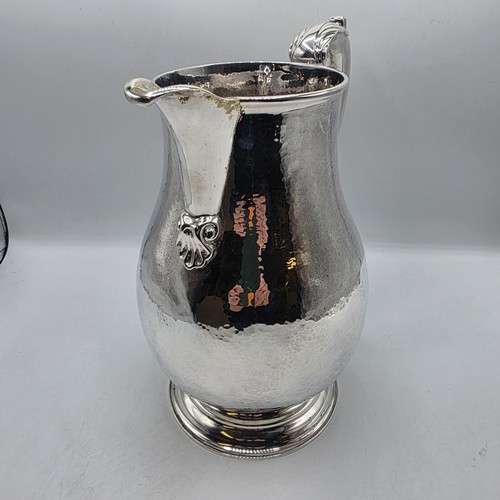 4 - A large Sterling silver hand planished water jug with cast scrolling handle on circular stepped foot... 