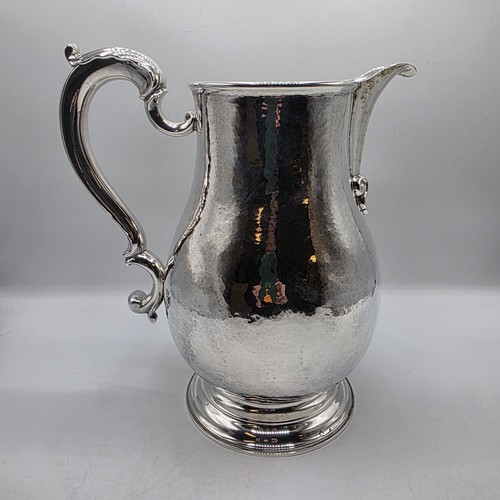4 - A large Sterling silver hand planished water jug with cast scrolling handle on circular stepped foot... 