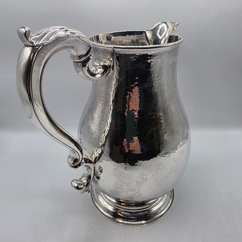 4 - A large Sterling silver hand planished water jug with cast scrolling handle on circular stepped foot... 