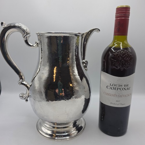 4 - A large Sterling silver hand planished water jug with cast scrolling handle on circular stepped foot... 