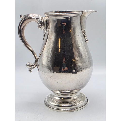 17 - A sterling silver hand planished water jug on circular stepped foot with scroll handle by SJ Phillip... 