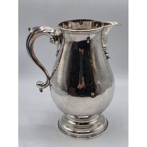 17 - A sterling silver hand planished water jug on circular stepped foot with scroll handle by SJ Phillip... 