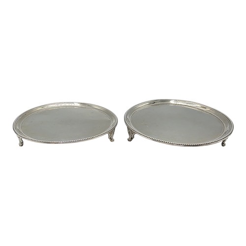 54 - A pair of sterling silver circular card trays or salvers with beaded rims on three shell feet.   Joh... 