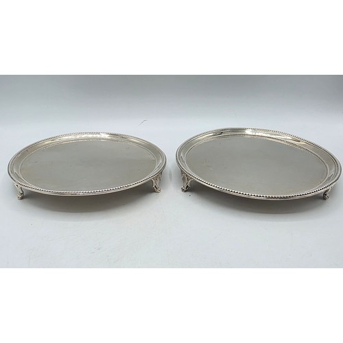 54 - A pair of sterling silver circular card trays or salvers with beaded rims on three shell feet.   Joh... 